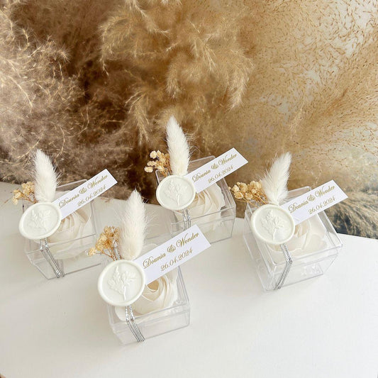 Cadeau invité : rose de savon Sisi en boîte plexi avec plume blanche, sceau décoratif et personnalisation des prénoms.