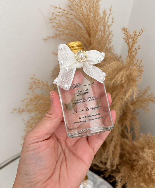 Eau de Zamzam Noor tenue à la main, détail du nœud en tissu perlé et du bouchon doré