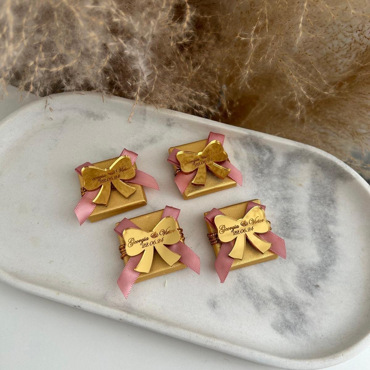 Boîte de dragées pour mariage, coloris doré avec ruban rose, personnalisée avec prénoms et date sur un nœud miroir