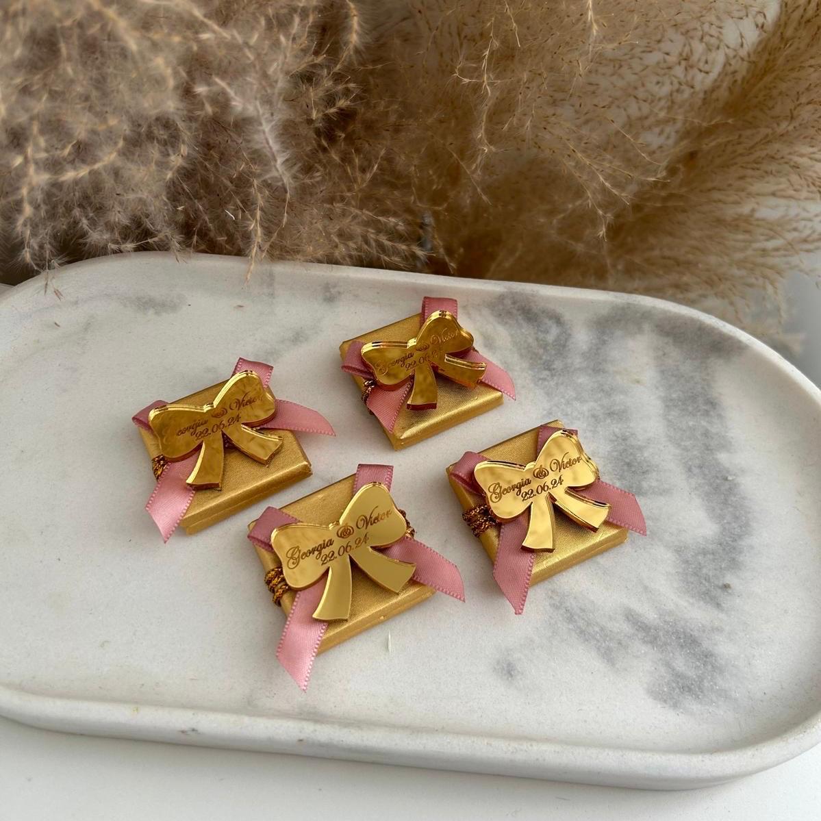 Boîte de dragées pour mariage, coloris doré avec ruban rose, personnalisée avec prénoms et date sur un nœud miroir