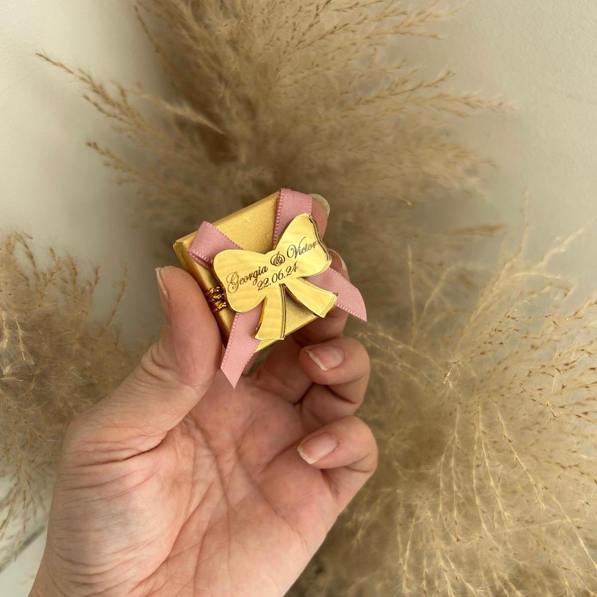 Boîte de dragées pour mariage, coloris doré avec ruban rose, personnalisée avec prénoms et date sur un nœud miroir