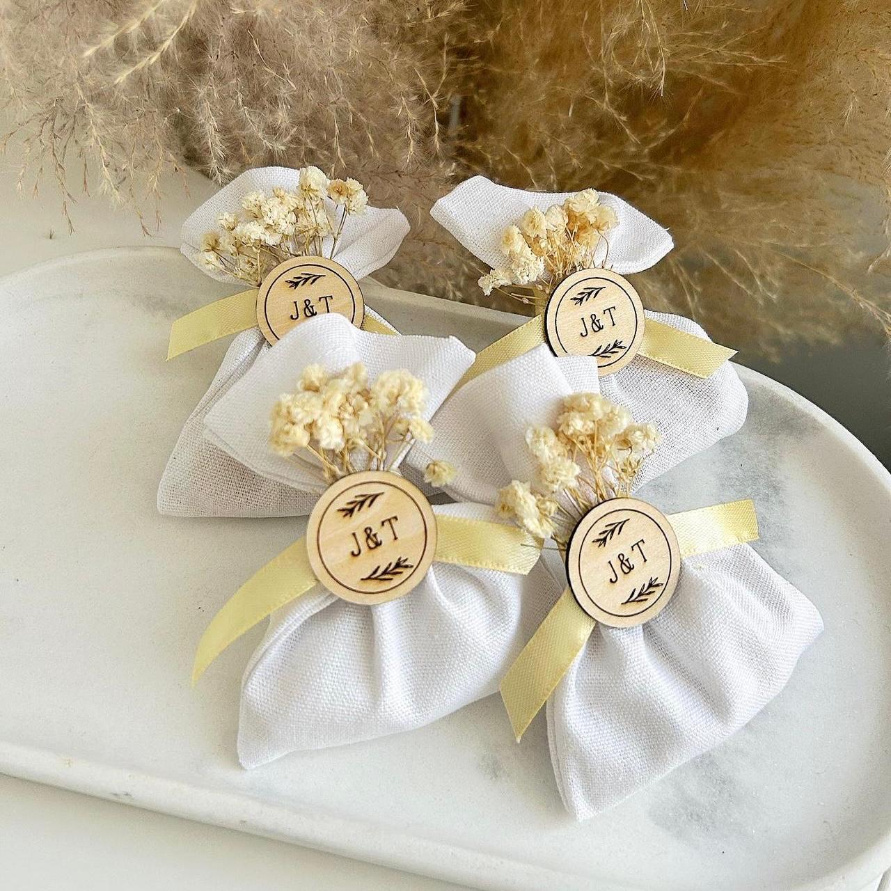 Cadeau invité : bourse de dragées rustique en tissu blanc avec fleurs séchées et médaillon en bois personnalisé.
