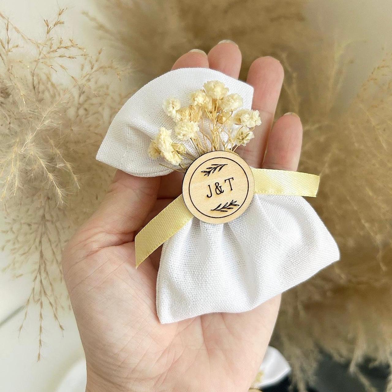 Cadeau invité : bourse de dragées rustique en tissu blanc avec fleurs séchées et médaillon en bois personnalisé.