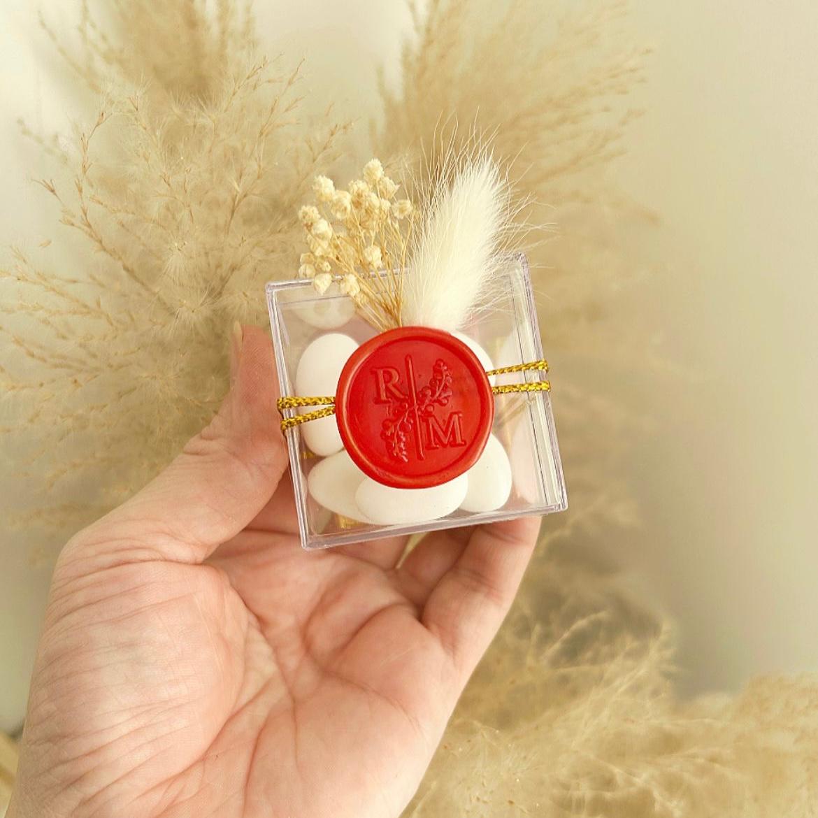 Cadeau invité : boîte de dragées Séduction en plexi avec sceau de cire rouge, ficelle dorée et décoration florale.