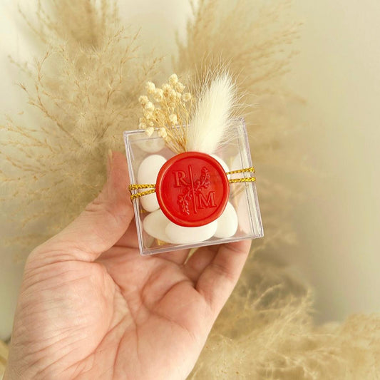 Cadeau invité : boîte de dragées Séduction en plexi avec sceau de cire rouge, ficelle dorée et décoration florale.