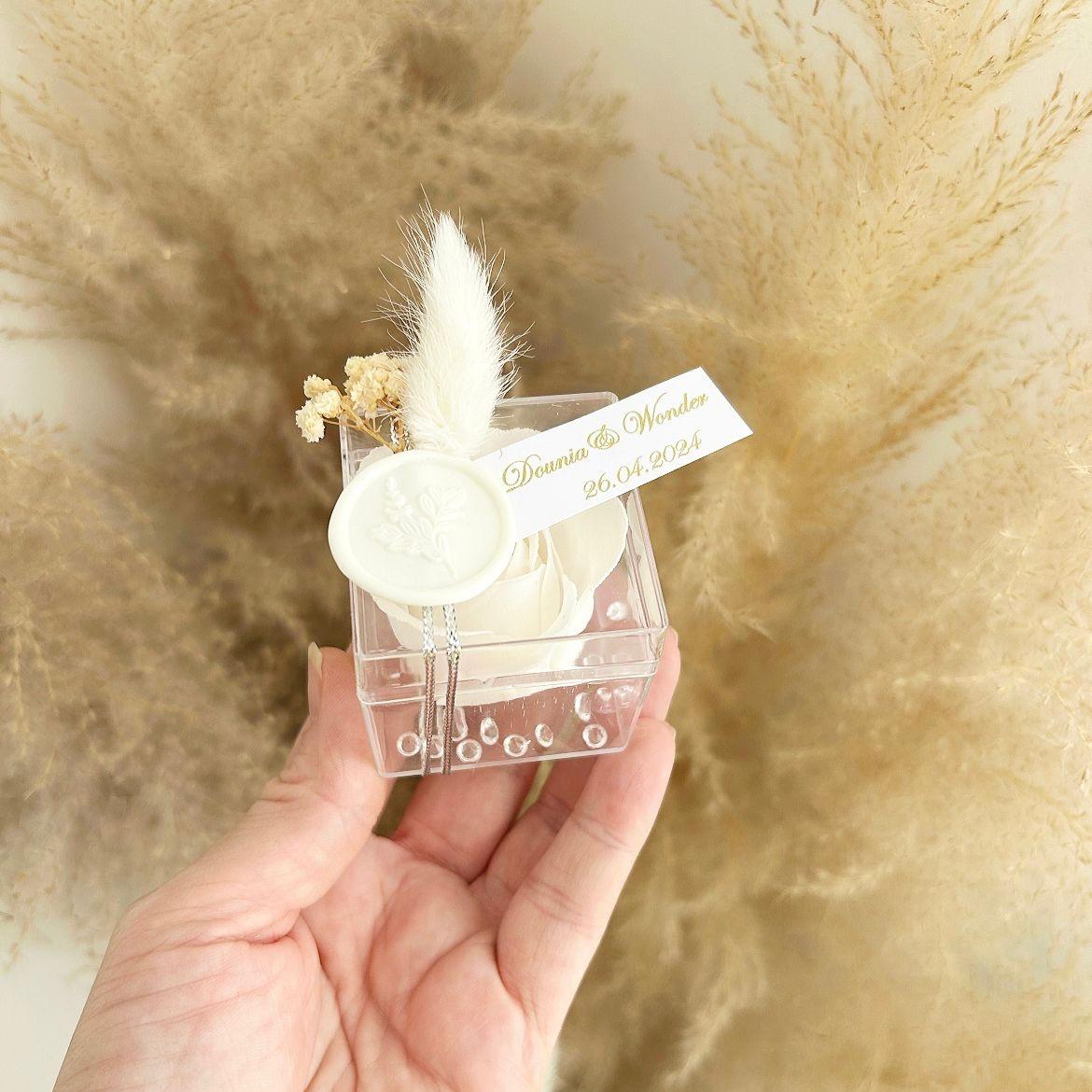 Cadeau invité : rose de savon Sisi en boîte plexi avec plume blanche, sceau décoratif et personnalisation des prénoms.