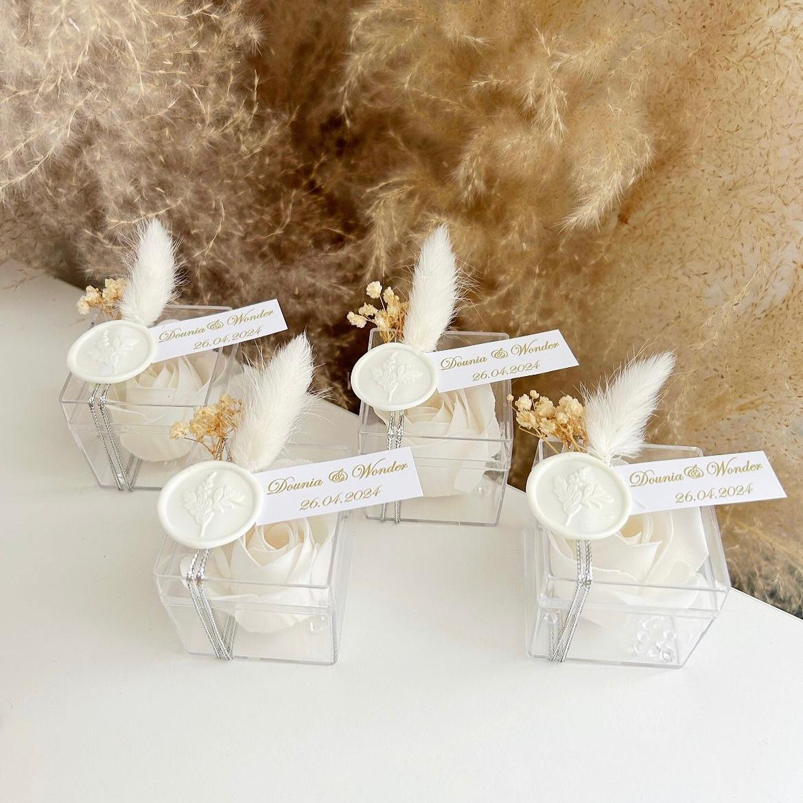 Cadeau invité : rose de savon Sisi en boîte plexi avec plume blanche, sceau décoratif et personnalisation des prénoms.